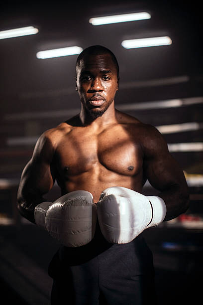 athletic boxer stands in gym lighting wearing white gloves, ready for training