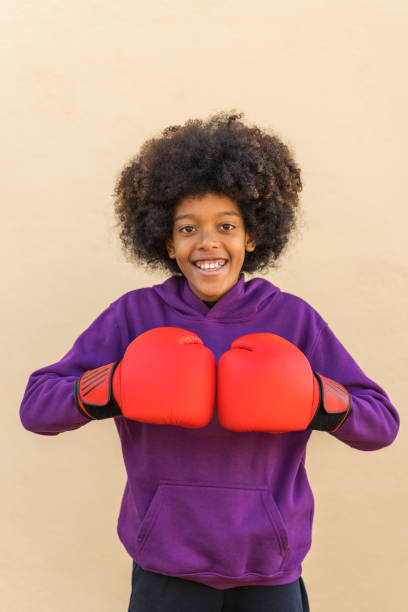 happy preteen boy practicing boxing against beige background