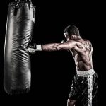 boxer training with punching bag on black background