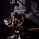 athlete in sleeveless top sits on bench in dim locker room, preparing gear