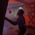 young black woman with boxing gloves punching a bag in box club in the evening